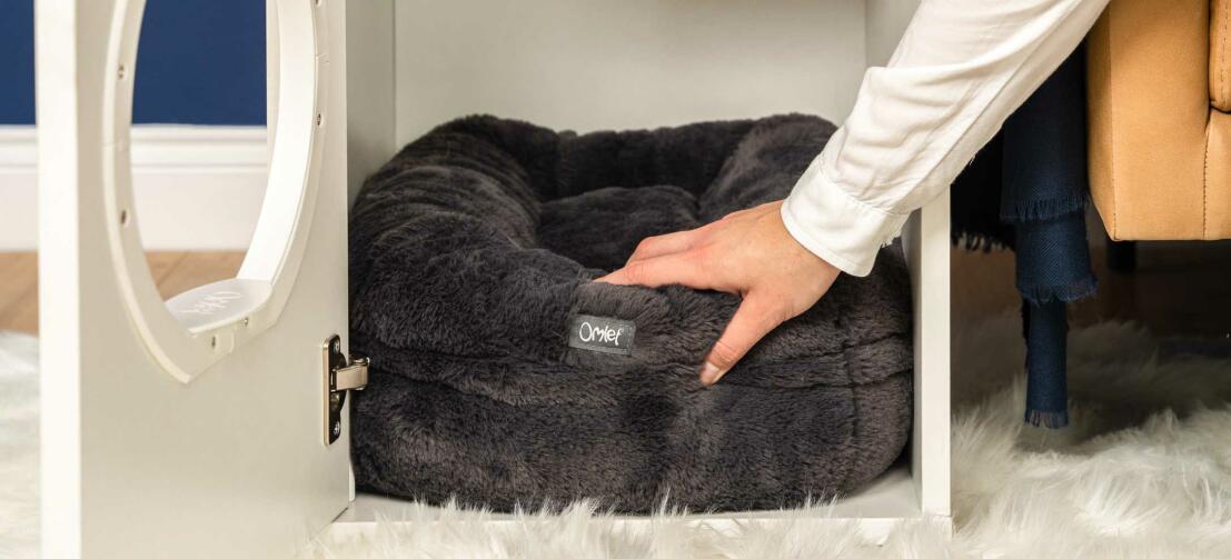 Persona che mette il letto per gatti nero Maya donut all'interno della casa per gatti Maya