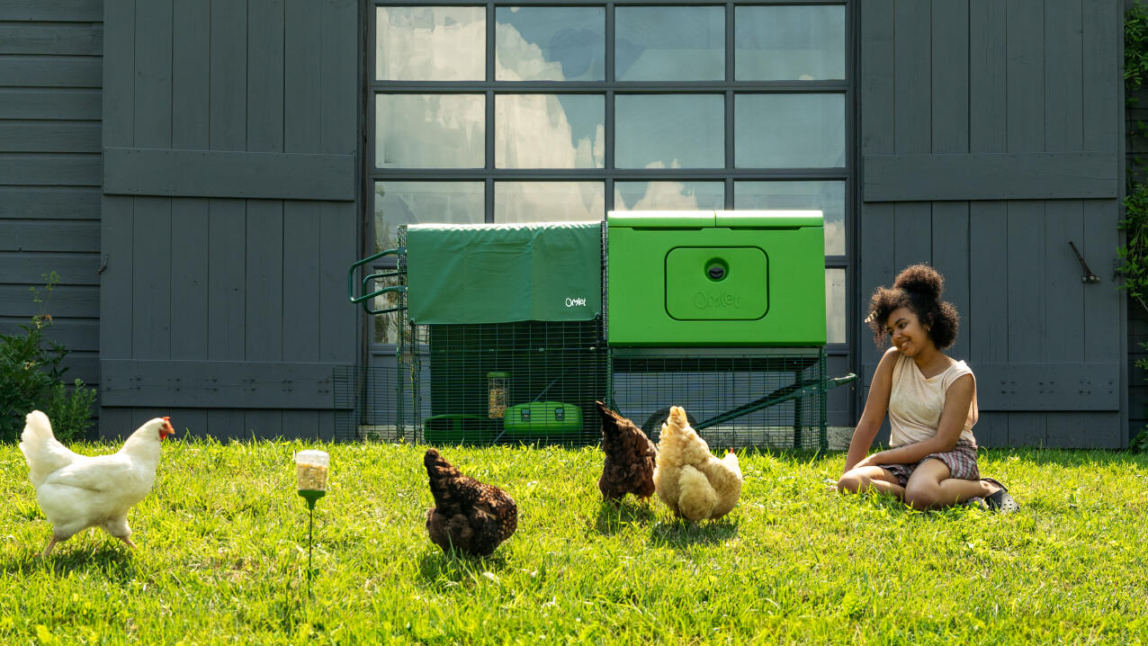 Donna seduta sull'erba accanto al suo pollaio a guardare le sue galline che razzolano