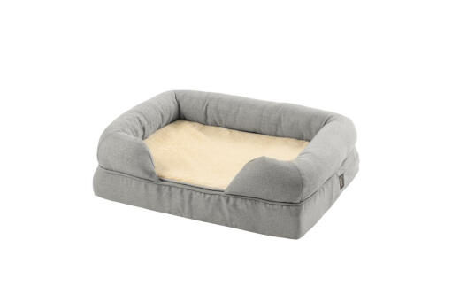 Un letto a bolster in memory foam grigio con una coperta di peluche piegata nel mezzo