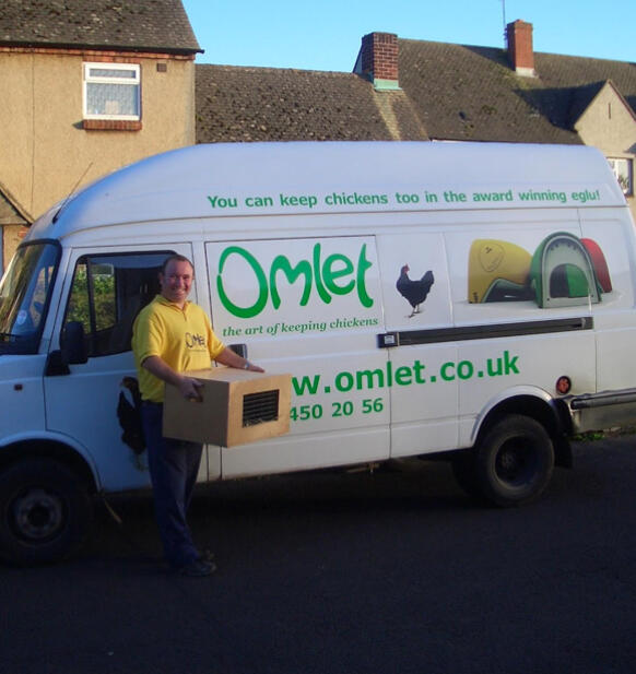 Un autista di consegne accanto a un furGone a marchio Omlet che trasporta una scatola di polli