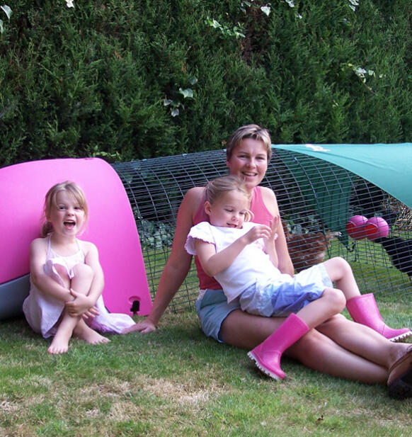 Una famiglia seduta accanto a un pollaio rosa Eglu 