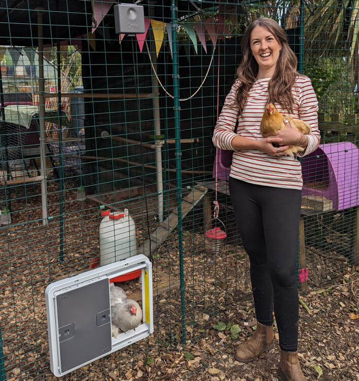 Donna che tiene in braccio una gallina davanti al suo pollaio con porta automatica