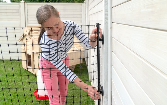 Donna che collega il recinto per galline di Omlet a un muro in legno nel suo giardino
